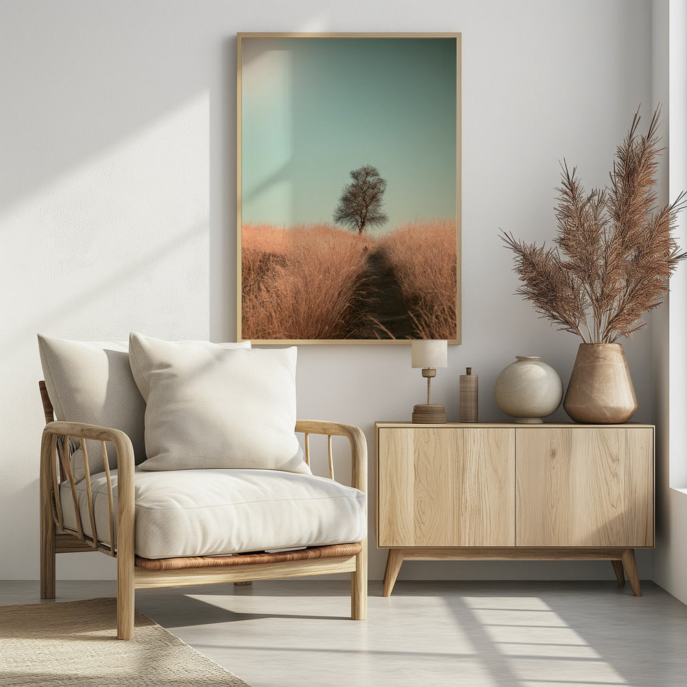 A minimalist photograph of a single bare tree standing alone on a gentle slope in a field of golden, dried grass under a clear, pale teal sky. A narrow path winds its way through the tall grass toward the tree. Print