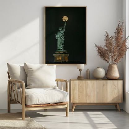 A striking night photograph of the Statue of Liberty, where a large, full yellow moon is perfectly aligned behind the torch, creating the illusion that the statue is holding up the moon. Artwork