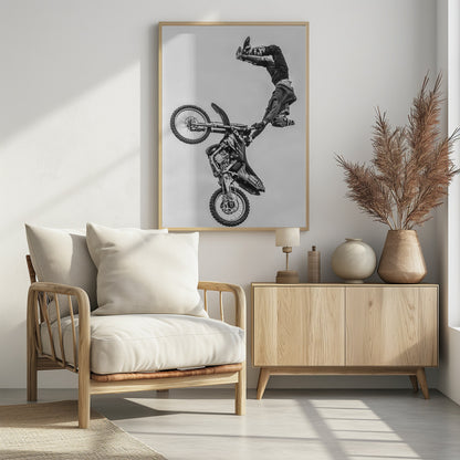 A dynamic black and white action shot of a freestyle motocross rider performing a handstand on the handlebars of their dirt bike mid-air. The bike is nearly vertical against a plain white sky, capturing a moment of extreme athleticism and balance. Poster