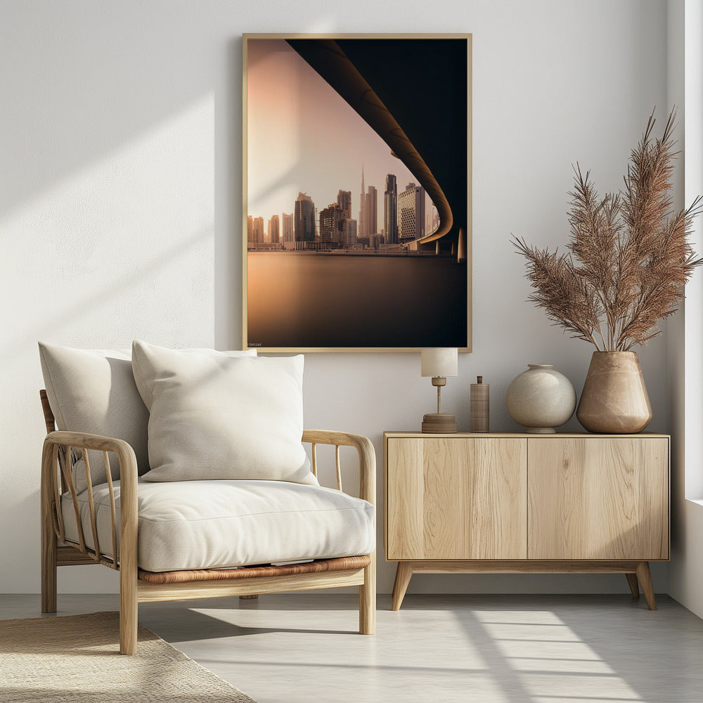 A view of the Dubai skyline, including the Burj Khalifa, framed by the sweeping curve of a bridge in the foreground. The city is bathed in the warm, soft light of a sunrise or sunset, with its reflection visible on the calm water below. Decor