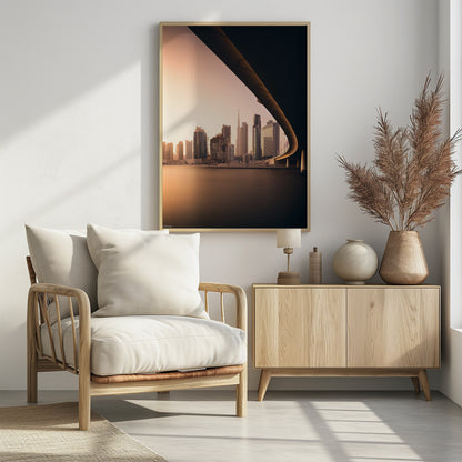 A view of the Dubai skyline, including the Burj Khalifa, framed by the sweeping curve of a bridge in the foreground. The city is bathed in the warm, soft light of a sunrise or sunset, with its reflection visible on the calm water below. Decor