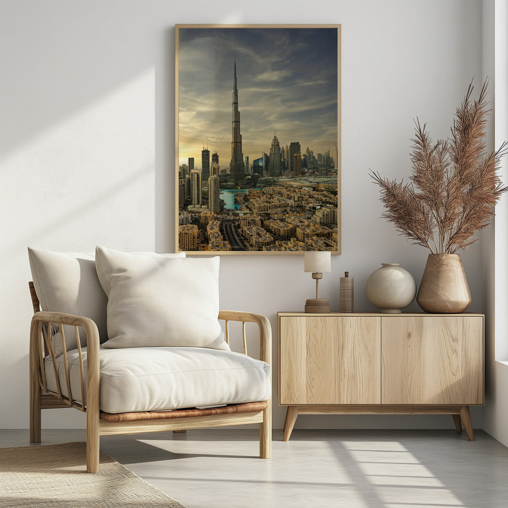 A framed photograph of the Dubai skyline at sunset, with the iconic Burj Khalifa skyscraper dominating the center. Surrounding it are numerous other modern high-rise buildings, a body of turquoise water, and a dense urban landscape in the foreground, all under a cloudy, golden-hued sky. Poster