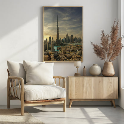 A framed photograph of the Dubai skyline at sunset, with the iconic Burj Khalifa skyscraper dominating the center. Surrounding it are numerous other modern high-rise buildings, a body of turquoise water, and a dense urban landscape in the foreground, all under a cloudy, golden-hued sky. Poster