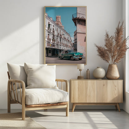 A vintage teal-green classic car sits on a sunny street in a historic city, possibly Havana, Cuba. Weathered apartment buildings with intricate balconies and hanging laundry line the street, with a peach-colored church tower visible in the background against a clear turquoise sky. Poster