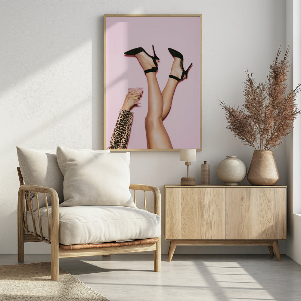 A woman's legs are kicked up in the air against a solid pink background. She is wearing black, pointed-toe, high-heeled shoes with ankle straps. A hand in a leopard print sleeve holds a pink, textured cocktail glass to the side. Artwork