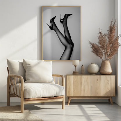 A black and white photograph of a woman's legs in the air, wearing sheer black stockings and shiny black stiletto high heels against a plain grey background. Poster