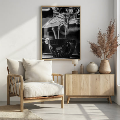 A close-up, black and white photograph of an espresso machine pouring two streams of fresh coffee from a chrome portafilter into a dark, glossy cup. Print