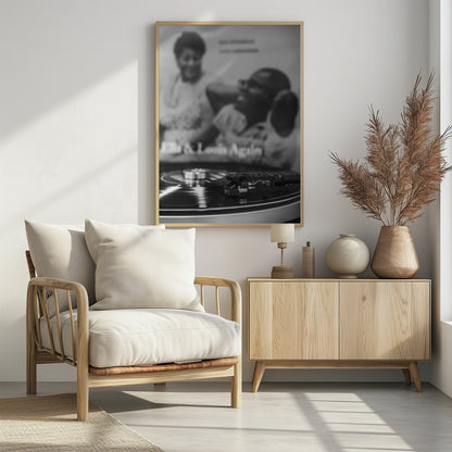 A black and white photograph focusing on a turntable's stylus resting on a spinning vinyl record. In the blurred background, the album cover for 'Ella & Louis Again' featuring Ella Fitzgerald and Louis Armstrong is visible. Poster