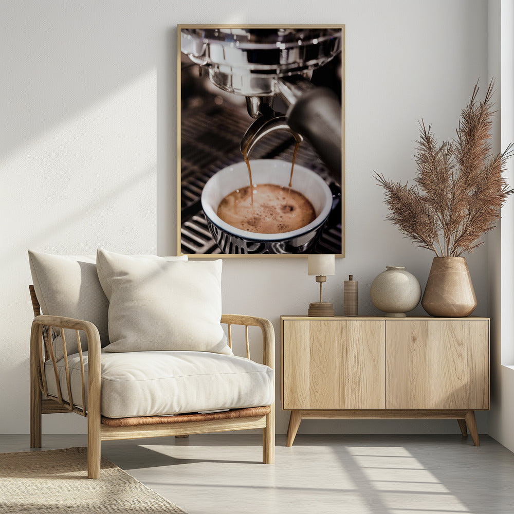 A close-up photograph of a shiny chrome espresso machine brewing a fresh shot of espresso. Two streams of rich, dark coffee pour from the portafilter into a white ceramic cup with a blue patterned rim, creating a light brown crema on top. Print
