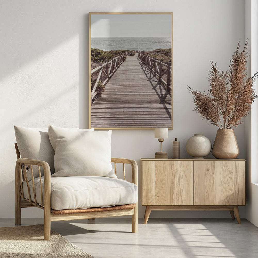 A long wooden boardwalk with rustic log railings leads the viewer's eye towards a calm, sunlit ocean under a hazy sky. Strong shadows from the railings fall across the path, creating a striped pattern. Poster