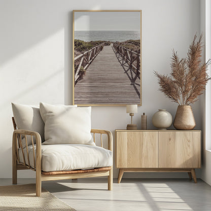 A long wooden boardwalk with rustic log railings leads the viewer's eye towards a calm, sunlit ocean under a hazy sky. Strong shadows from the railings fall across the path, creating a striped pattern. Poster