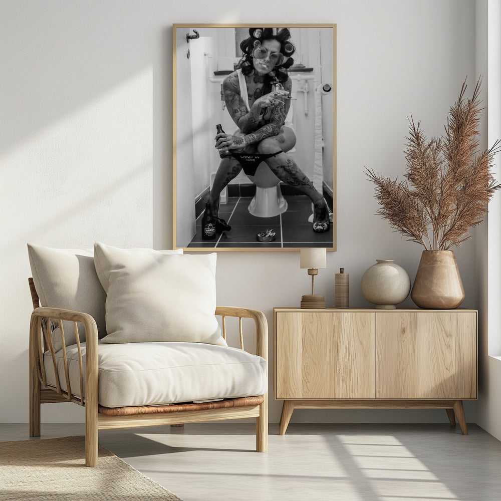 A black and white photo of a heavily tattooed woman with her hair in rollers sitting on a toilet. She wears large sunglasses, smokes a cigarette, holds a beer bottle, and has on black underwear that says 'CRAZY IN LOVE'. An ashtray and another beer bottle are on the floor. Artwork