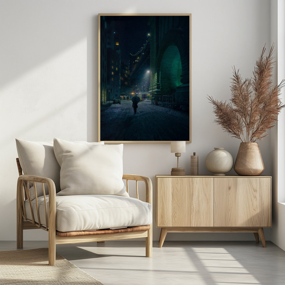A lone person holding an umbrella walks down a snow-covered street at night, dwarfed by the massive, green-lit stone archway of the Brooklyn Bridge as snow falls around them. Print