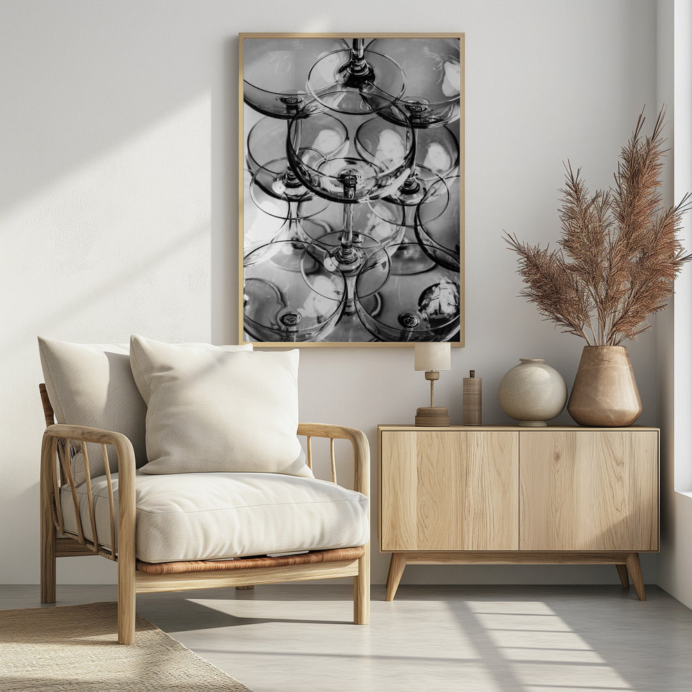 A black and white, overhead photograph of a tightly packed stack of empty champagne coupe glasses. The overlapping rims, stems, and bowls create a complex abstract pattern of circles and reflections, all enclosed within a simple black frame. Poster
