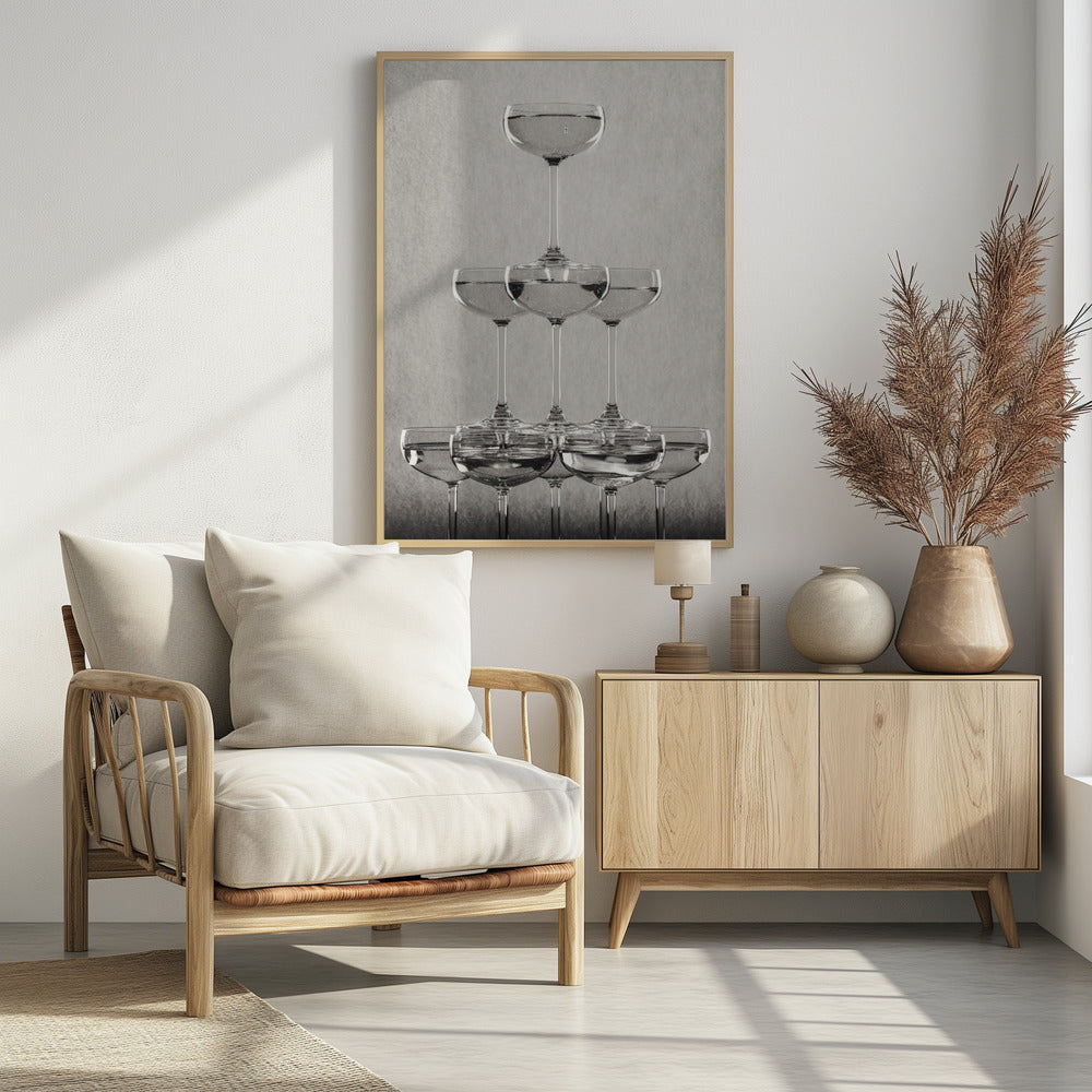 A classic black and white photograph of a champagne tower, with coupe glasses stacked in a pyramid. The glasses are filled with bubbly liquid, and the composition is set against a textured light gray background and enclosed in a black frame. Poster