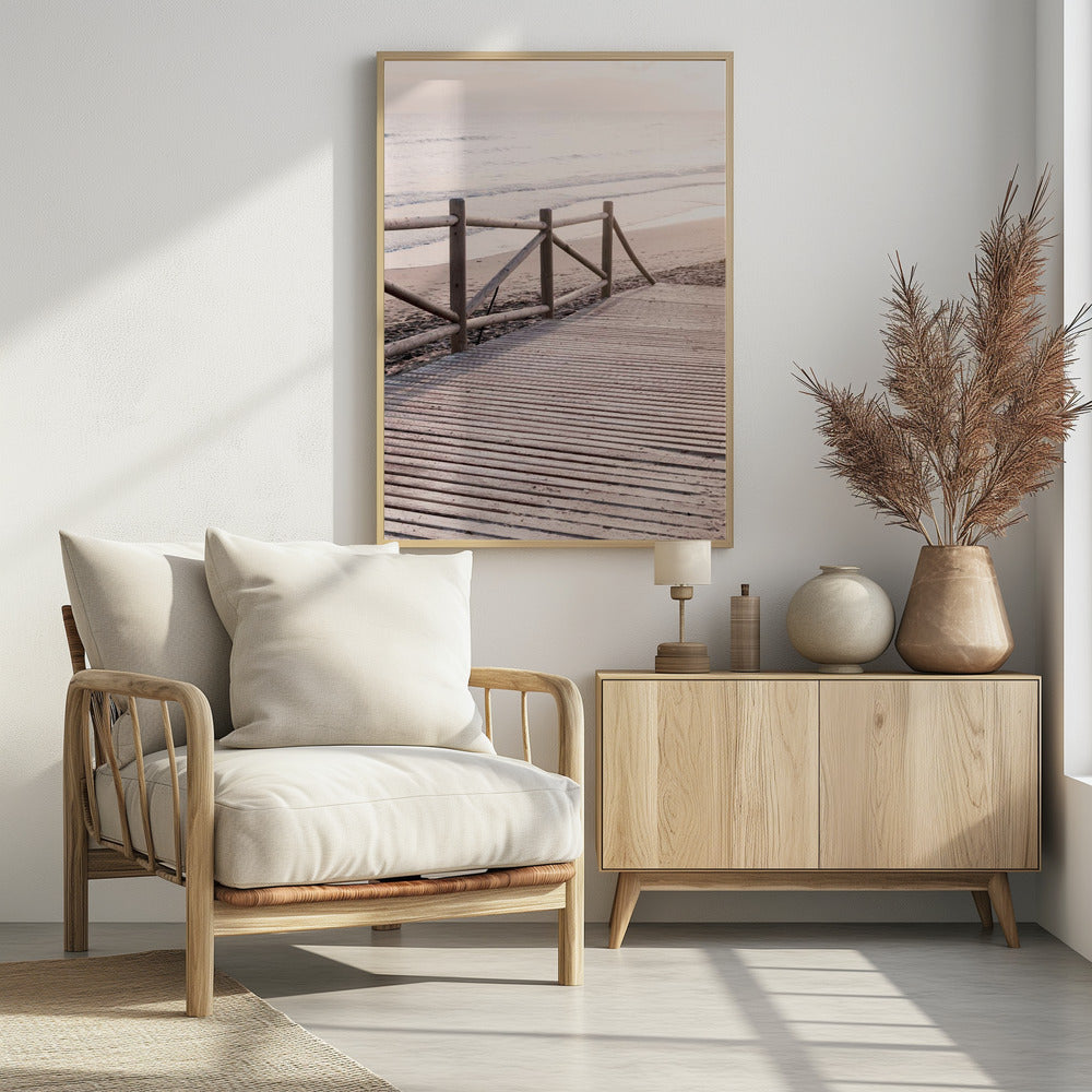 A wooden boardwalk with a rustic log fence leads down to a sandy beach with gentle waves lapping at the shore under a soft, hazy sunrise or sunset. Decor