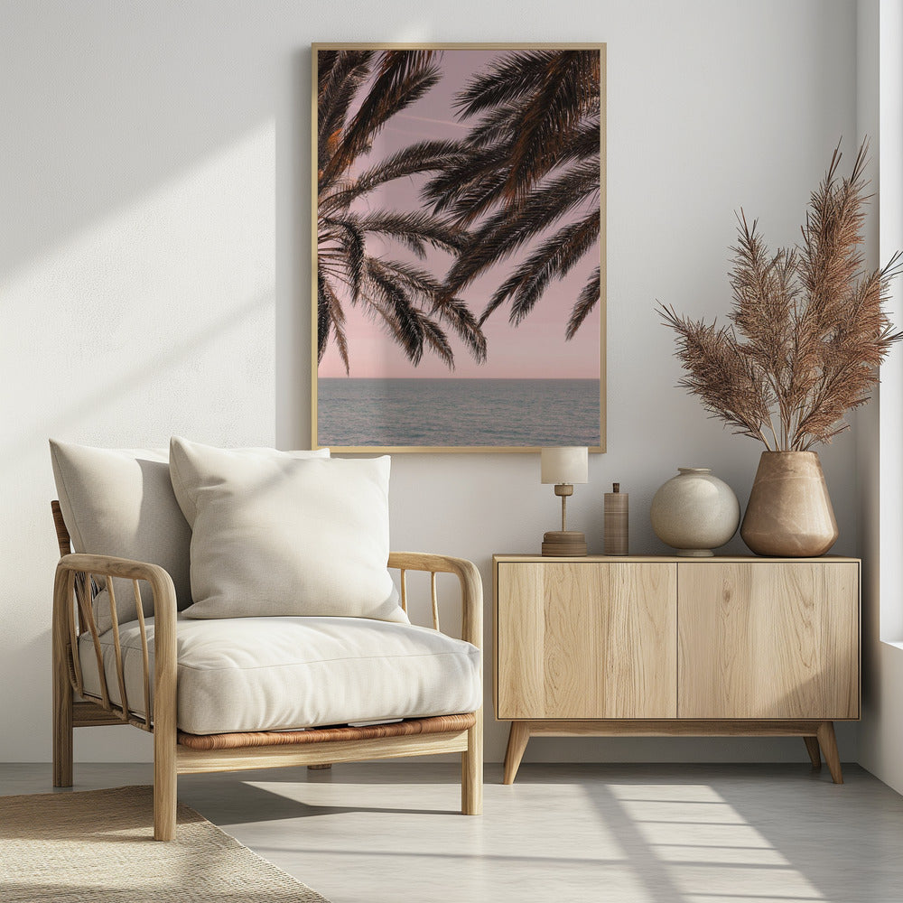 Dark palm tree fronds hang over a calm teal ocean under a soft pink sky, creating a serene and tropical atmosphere. The view is from under the palm tree looking out towards the water. Artwork