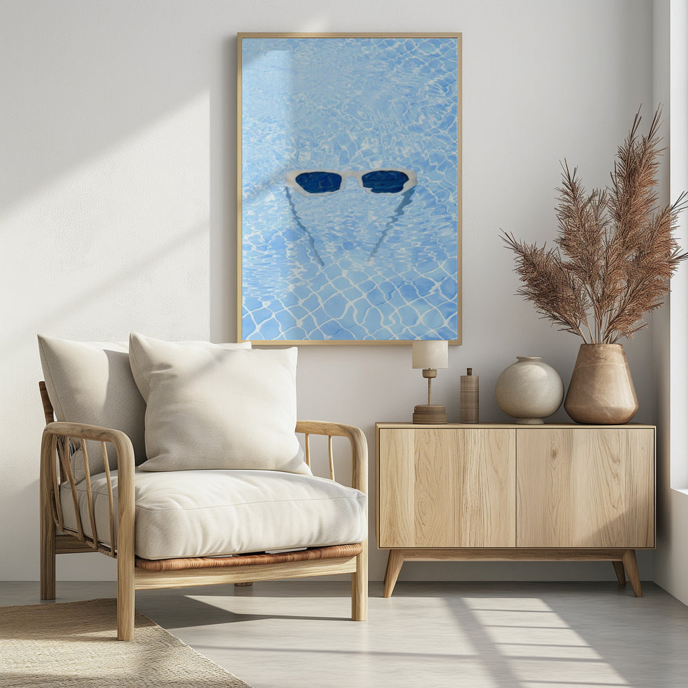 A pair of white-framed sunglasses with dark lenses floats on the surface of a bright blue swimming pool. The rippling water distorts the view of the tiled pool floor, and the sunglasses cast a faint shadow underneath. Print