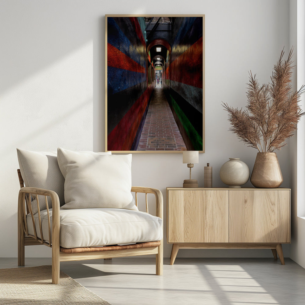 A long, narrow brick alleyway viewed from a one-point perspective, with walls painted in wide, colorful horizontal stripes of red, blue, and black, leading to a distant, sunlit exit where a person stands. Wall Art