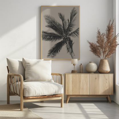 A low-angle, monochrome photograph of a palm tree against a solid light beige sky. The image is framed in black, and the palm fronds spread out across the frame, with a few coconuts visible at the top of the trunk. Poster