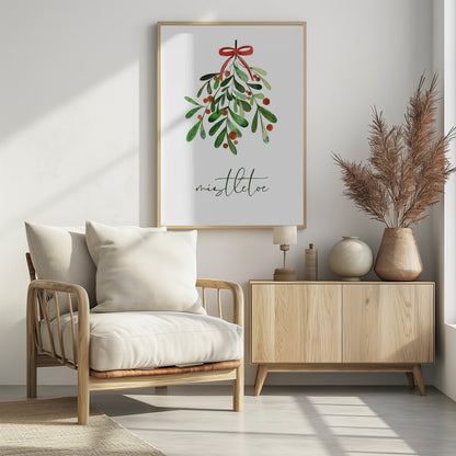 A framed watercolor illustration of a sprig of mistletoe with green leaves and red berries, tied with a red bow. Below the plant, the word 'mistletoe' is written in a cursive script on a clean white background. Artwork