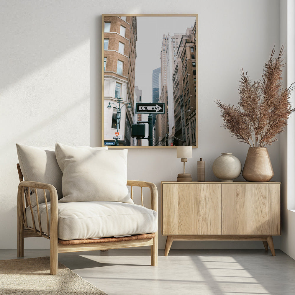 A framed photograph of a New York City street, with a prominent 'ONE WAY' sign in the foreground pointing right. The view is from a low angle, looking up between tall brick and stone buildings towards a bright, overcast sky. Wall Art