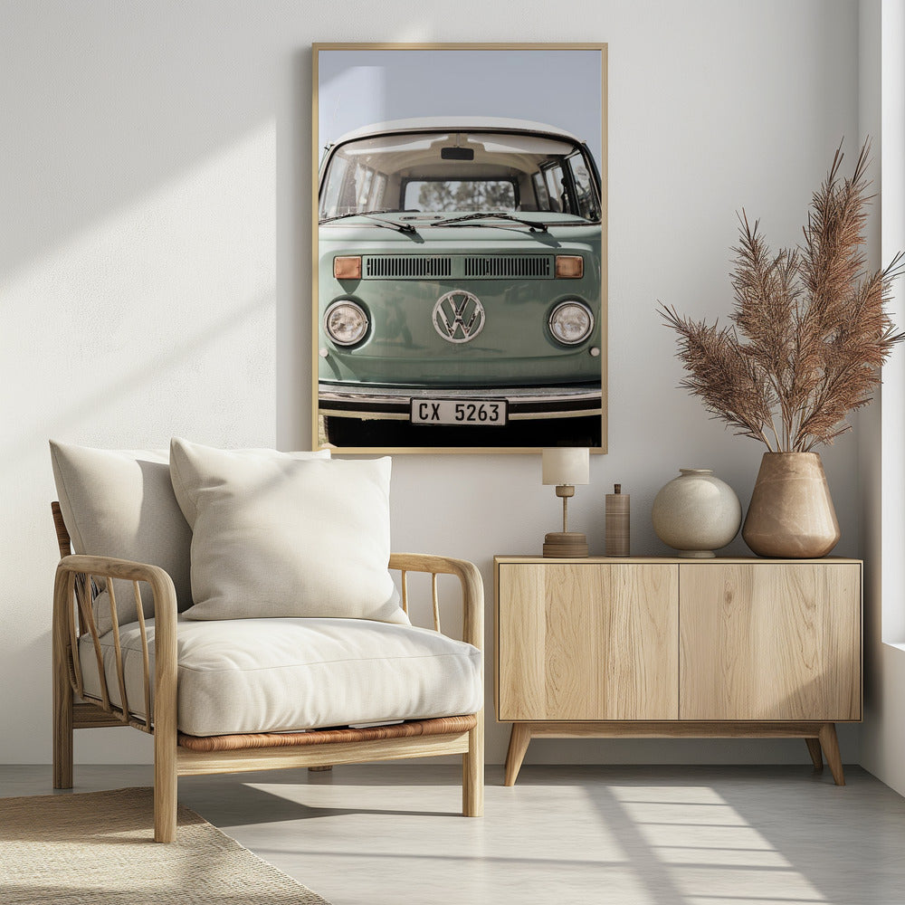 A close-up front view of a vintage sage green Volkswagen bus with a white roof. The iconic VW logo is on the front, with round headlights and a European license plate, set against a pale blue sky. Print