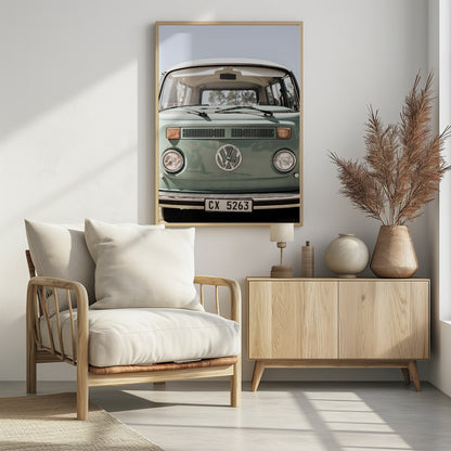 A close-up front view of a vintage sage green Volkswagen bus with a white roof. The iconic VW logo is on the front, with round headlights and a European license plate, set against a pale blue sky. Print