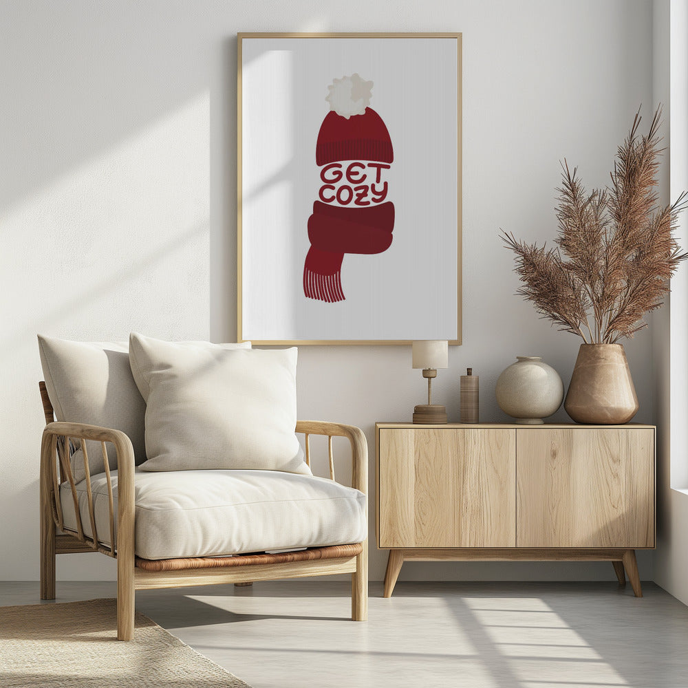 A minimalist illustration of a red knit beanie with a white pom-pom and a matching red scarf. The words 'GET COZY' are written in a playful font, forming the middle section of the hat and scarf against a plain white background, enclosed in a black frame. Poster