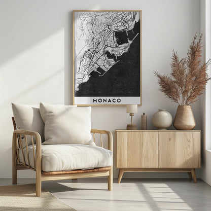 A modern black and white map of Monaco, presented as a framed poster. The map details the city's streets and coastline in black lines on a white background, while the sea is depicted in a solid, textured black. The title 'MONACO' is at the bottom in a bold, white band. Poster