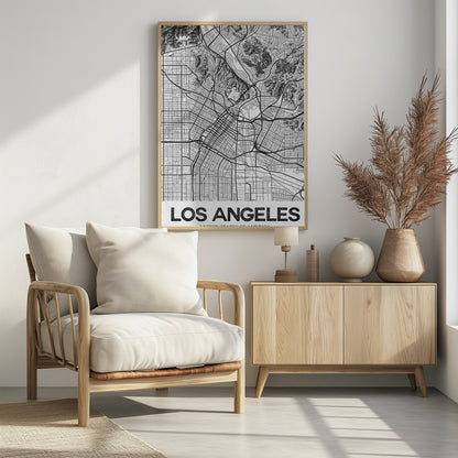 A modern, framed black and white map of Los Angeles. The detailed illustration features a dense grid of city streets, winding highways, rivers, and topographic details of hills. A white banner at the bottom displays the words 'LOS ANGELES' in a bold, black, textured font. Poster