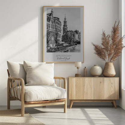 A black and white travel poster of Amsterdam, Netherlands. The photo shows the Munttoren clock tower and traditional Dutch buildings along the Singel canal. A floating barge filled with bicycles is in the foreground. The poster has a white border with the text 'AMSTERDAM', 'De Munt, Singel', and 'NEDERLAND' at the bottom. Artwork