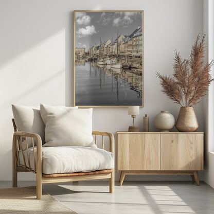 A muted, desaturated photograph of the Nyhavn harbor in Copenhagen. Old-fashioned sailboats are moored along the canal in front of a row of colorful historic buildings. The boats, buildings, and a cloudy sky are perfectly reflected in the calm water. Wall Art