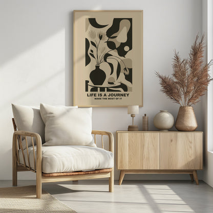 A framed abstract art print in a neutral color palette. It depicts a stylized still life with a dark vase of flowers on a table, set against a background of large, organic shapes in beige, taupe, and dark brown. Below the image, the motivational quote 'LIFE IS A JOURNEY' and 'MAKE THE MOST OF IT' is printed in a bold, dark font. Artwork