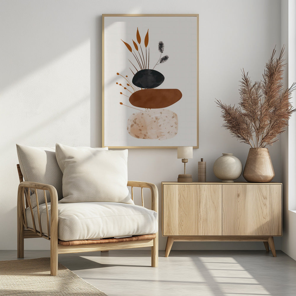 A minimalist abstract artwork featuring a stack of three organic, stone-like shapes against an off-white background, framed in black. The bottom shape is a speckled beige, the middle is a solid terracotta brown, and the top is a textured charcoal black. Various stylized botanical elements, including brown reeds and black fuzzy stems, emerge from behind the stack. Decor