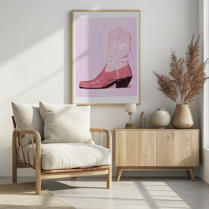 A framed art print of a pink cowboy boot against a light pink, textured background. The boot is illustrated in a block-print style with shades of pink, white decorative inlay patterns of moons and stars, and a dark brown heel and sole. Decor