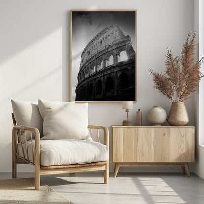 A dramatic, low-angle black and white photograph of the ancient Roman Colosseum. The sun shines brightly through one of the upper archways, creating a lens flare and silhouetting a few birds in flight against the cloudy sky. Poster