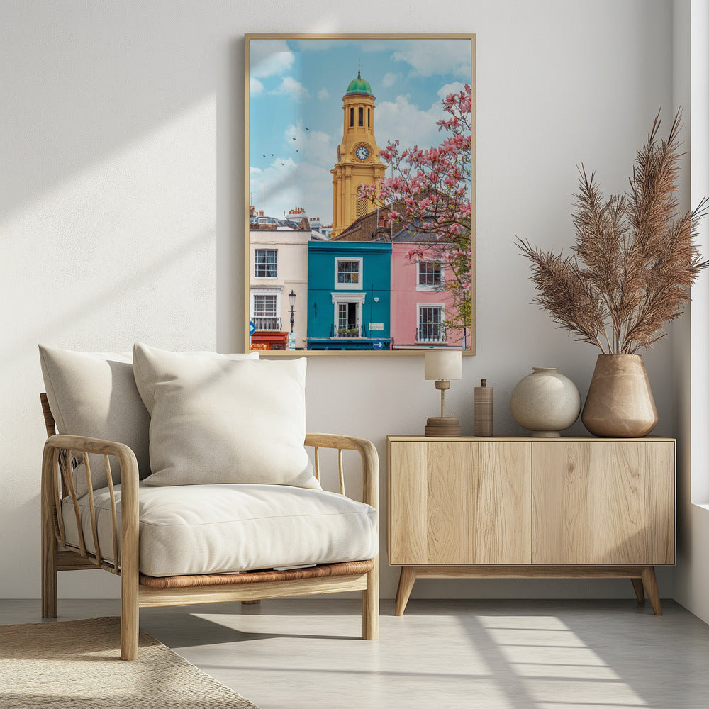 A vibrant city street scene on a sunny day, featuring a row of colorful houses in teal, pink, and off-white. A striking yellow clock tower with a green dome stands tall against a bright blue sky, with a blooming pink magnolia tree in the foreground. Print