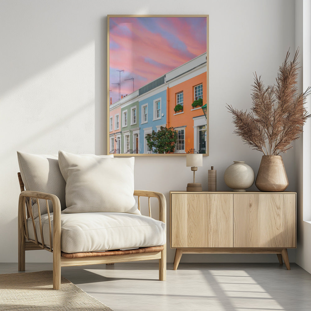 A row of colorful pastel townhouses in shades of orange, blue, green, and pink, viewed from a low angle against a dramatic, cloudy pink and purple sunset sky. Poster