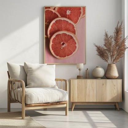 A close-up photograph of several overlapping slices of vibrant pink grapefruit arranged on a pale pink surface, enclosed within a simple black frame. Print