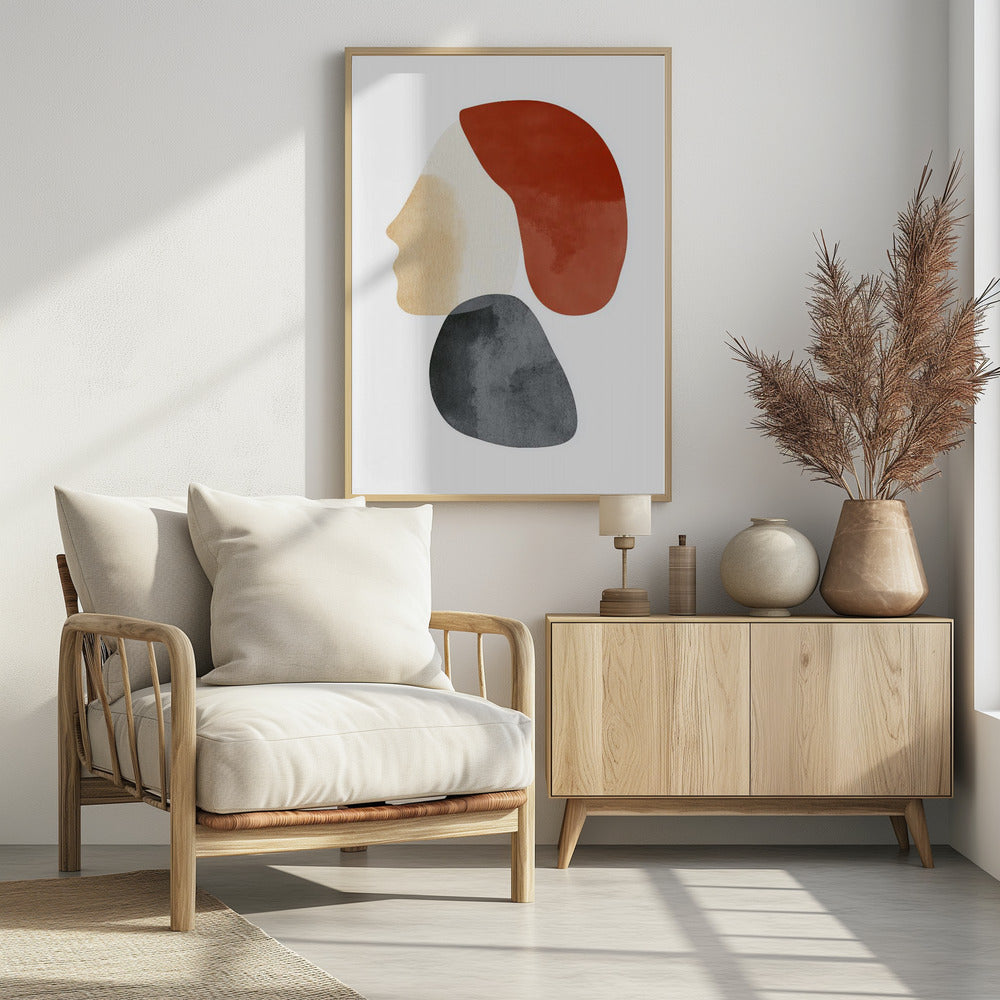 A minimalist abstract artwork in a black frame, featuring overlapping shapes that form a stylized human profile. The face is a light beige, topped with a rust-red shape like hair, and a dark grey, stone-like shape is positioned below the chin, all on a white background. Artwork