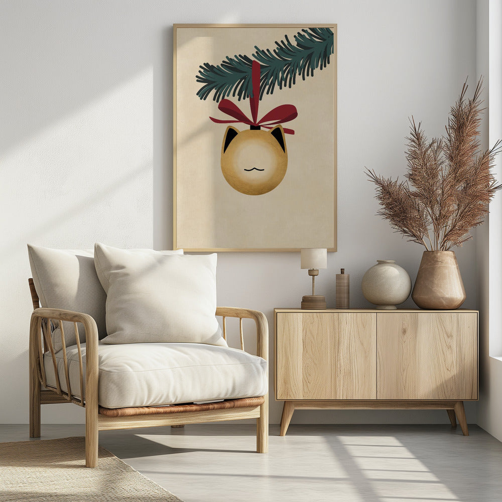 A minimalist illustration of a golden-yellow Christmas ornament shaped like a cat's head, complete with black-tipped ears and a simple line mouth. It hangs from a dark green pine branch by a festive red ribbon, all set against a textured beige background and framed in black. Artwork