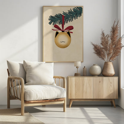 A minimalist illustration of a golden-yellow Christmas ornament shaped like a cat's head, complete with black-tipped ears and a simple line mouth. It hangs from a dark green pine branch by a festive red ribbon, all set against a textured beige background and framed in black. Artwork