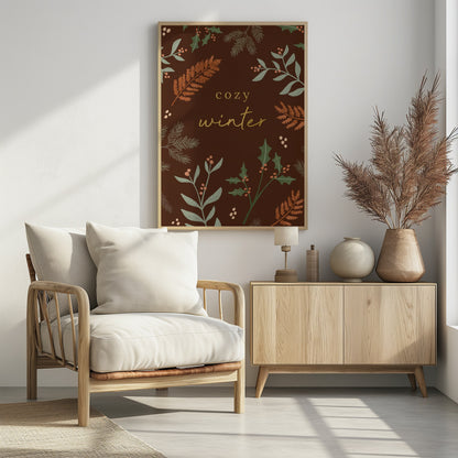A warm, illustrative poster with a dark brown background featuring the words 'cozy winter' in gold script at the center. The text is framed by a wreath of winter botanicals, including holly, pine needles, and ferns in shades of green and burnt orange. Print