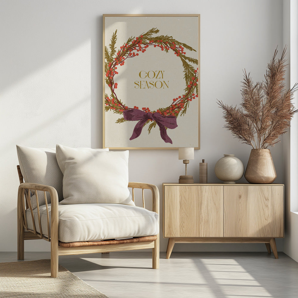 A vintage-style illustration of a festive wreath made of green boughs and red berries, tied with a large purple bow at the bottom. The text 'COZY SEASON' is written in gold inside the wreath on a cream-colored background, all enclosed in a thin black frame. Wall Art