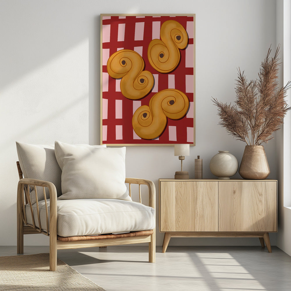 A vibrant illustration of three golden-yellow S-shaped pastries, resembling Swedish saffron buns, resting on a red and pink checkered tablecloth. The artwork is presented within a black frame. Decor