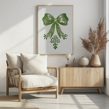 A vintage-style linocut print of a large green bow with leafy accents on a white background, enclosed in a thin black frame. The bow is detailed with lines suggesting texture and shadow, and foliage hangs from its ribbons. Artwork
