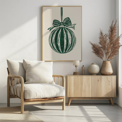 A vintage-style linocut print of a dark green Christmas bauble with a large bow, hanging against a cream background. The ornament features vertical stripes and white speckles, and the entire artwork is presented in a simple black frame. Artwork