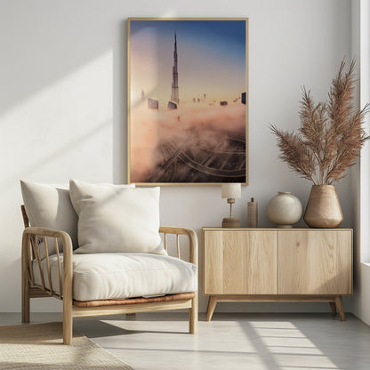 An aerial photograph of the Burj Khalifa in Dubai, towering over a thick blanket of pink and orange-hued fog at sunrise. Below the fog, a complex highway interchange is visible, with the clear blue sky above. Wall Art