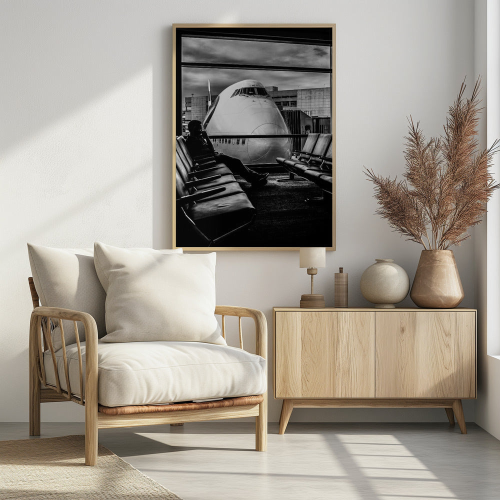 A dramatic black and white photograph of a silhouetted person sitting in an airport departure lounge, waiting for their flight. Through the large window, the enormous nose of a Boeing 747 jumbo jet is visible up close, dominating the view under a cloudy sky. Artwork